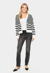 Cardigan rayé noir et blanc avec un col en V, coupe décontractée, poignets côtelés, associé à un jean sombre et des escarpins noirs à bout pointu.