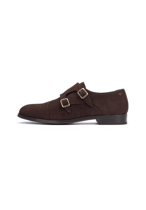 Zapato de vestir de ante marrón con dos hebillas decorativas, punta afilada, tacón bajo y textura suave. Diseño simple con una marca sutil en el lateral.