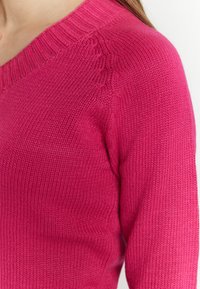 Maglione a maglia fucsia con scollatura a V, colletto a costine e dettagli in punto testurizzato sulle spalle. Tessuto morbido e leggero.