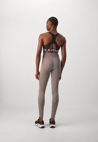 Black racerback sports bra with bold logo, paired with light gray ribbed leggings and black athletic shoes. Smooth texture, fitted design.