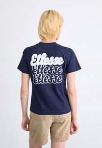 T-shirt bleu marine avec un grand logo blanc "Ellesse" au dos. Manches courtes, col rond, fabriqué en coton avec une texture lisse.