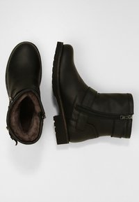 Bottines en cuir noir avec une surface texturée, semelle en caoutchouc plate, fermeture éclair sur le côté et une doublure en fourrure confortable visible à l'intérieur.