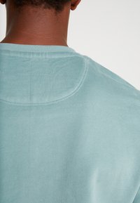 Sudadera azul claro con cuello redondeado y textura suave. Presenta costuras visibles a lo largo del cuello y la zona del hombro.