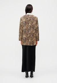 Μπλέιζερ με λεοπάρ σχέδιο και άνετη εφαρμογή, με αντίθετο λευκό γιακά, συνδυασμένο με μαύρη σατέν φούστα και μυτερές μαύρες μπότες.