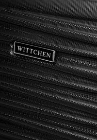 Sac de voyage noir avec une texture tissée, un design zippé et une plaque en métal argenté embossée avec "WITTCHEN."
