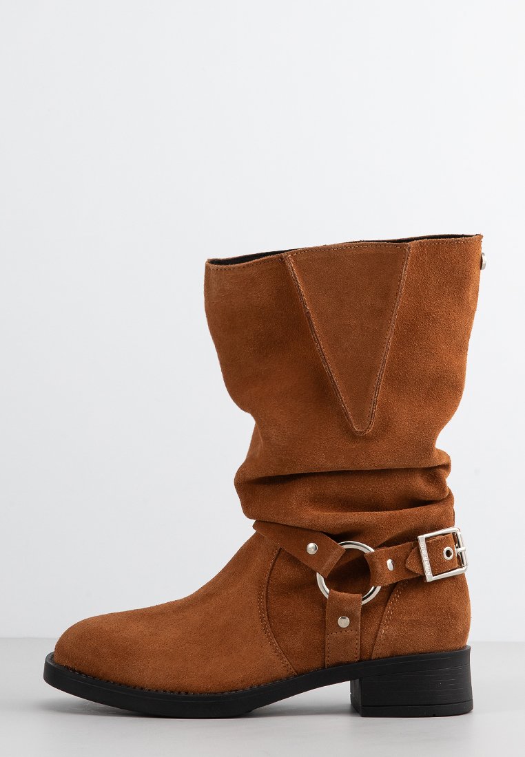 Braune Wildleder-Stiefelette mit lässigem Design, runder Spitze und einem Riemen mit silberner Hardware-Akzent. Blockabsatz für zusätzlichen Halt.