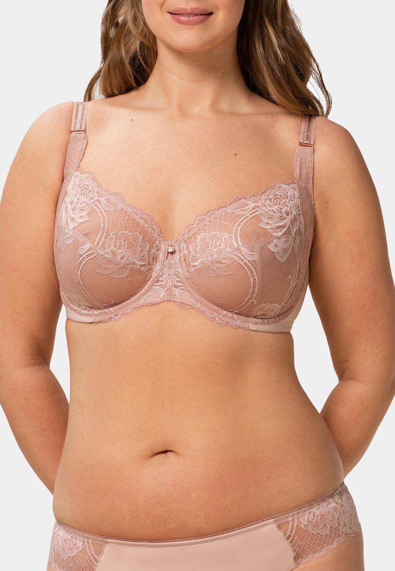 Podprsenka s krajkovým lemováním v broskvové barvě, zdobená květinovými vzory, s nastavitelnými ramínky a malým drahokamem uprostřed. Jemný, průsvitný materiál.