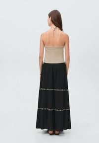 Maxi dress with a fitted beige bodice and a black skirt. The skirt features embroidered accents and a flowy texture. Open back design.