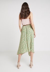 Blommig midikjol med ett grönt och rosa mönster, lätt tyg, asymmetrisk fåll, kombinerad med en ljusrosa topp och beige skor med blockklack.