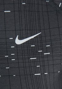 Tissu de sport noir avec un motif en grille, comportant un logo Nike blanc et des lignes blanches alternées pour des accents de design.