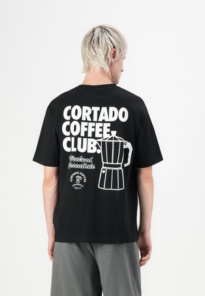 T-shirt en coton noir avec du texte blanc et un graphique d'une cafetière au dos. Manches courtes, coupe décontractée, design simple.