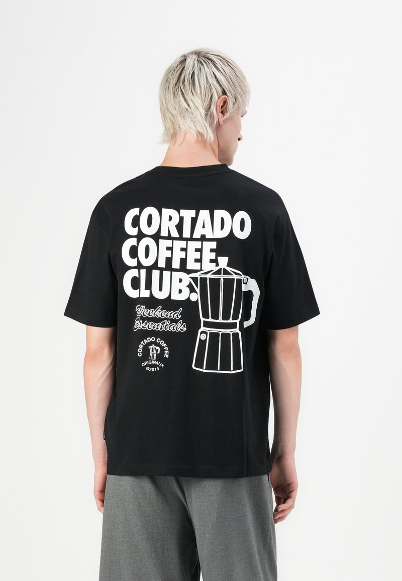Schwarz Baumwoll-T-Shirt mit weißem Text und einem Grafikmotiv eines Kaffeeautomaten auf dem Rücken. Kurze Ärmel, lockere Passform, einfaches Design.