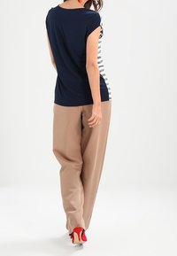 Camiseta a rayas en azul marino y blanco con mangas cortas, combinada con pantalones de pierna ancha beige y tacones rojos, vista desde la espalda.