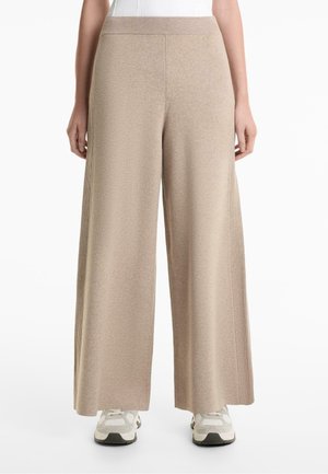 Beige wide-leg pants made of soft knit material, featuring a ribbed waistband and side detailing. Paired with gray athletic shoes.