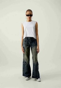 Witte mouwloze top met kantdetails, gecombineerd met wijde, donkerdenim cargobroeken met voorzakken en lichte vervaging. Witte sneakers inbegrepen.