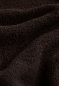 Mørkebrunt tekstureret stof med en blød, fluffy overflade, der har blide folder og bølger, der fremhæver dets varme og dybde.