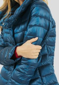 Blå dunjakke med quiltet mønster, høj krave og lynlås foran. Materialet virker skinnende og glat, med en mat indvendig foring.