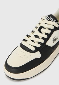 Fekete és krémszínű sneaker, texturált bőrből készült felsőrésszel, perforált orral, vastag fűzőkkel és hímzett logóval az oldalon.