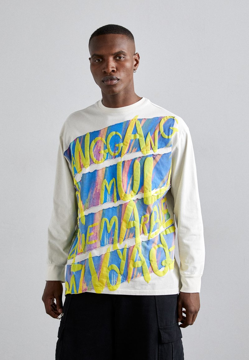 Tricou alb cu maneci lungi, prezentând un text abstract colorat în galben și albastru. Tricoul are o croială lejeră și o textură moale a materialului.
