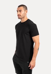 Camiseta de algodón negra con cuello redondo y mangas cortas, llevada por un modelo, textura suave y corte regular.