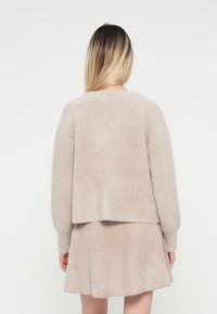 Puhavás beige pulóver, laza szabással, eső vállvarrásokkal, a hátsó hossza enyhén rövidebb, mint az elülső része, egy passzoló szoknyával párosítva.