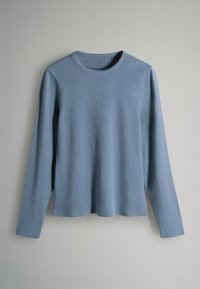Langärmliges hellblaues Hemd aus geripptem Stoff, mit Rundhalsausschnitt und seitlichen Schlitzen am Saum für mehr Bewegungsfreiheit.