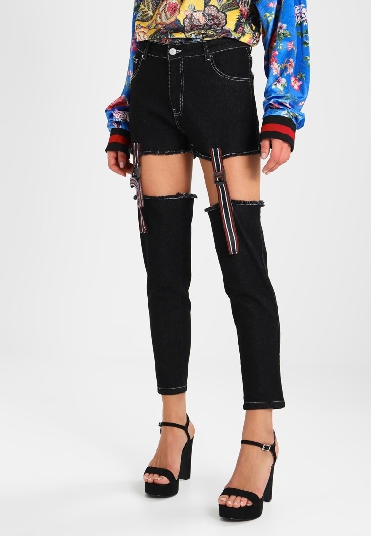 Högmidjade, svarta denimshorts med utskurna sektioner ovanför knäna, med randiga accenter och slitna kanter. Plattformsskor i svart.