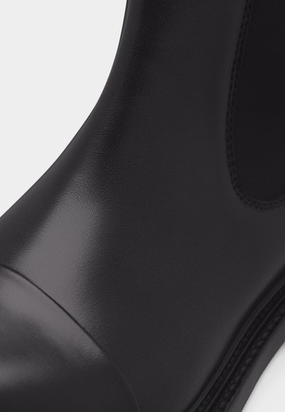 Λείο μαύρο δερμάτινο μποτάκι με ελαστική πλαϊνή πινελιά και στρογγυλεμένη μύτη, που δείχνει λεπτομερή υφή και ραφές στο επάνω μέρος.