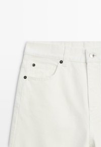 Vita jeans i denim med klassisk femficksdesign, nitdetaljer och en mjuk, texturerad yta. Midjebandet har knappstängning.