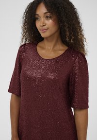 Burgundijska haljina sa šljokicama, kratkim rukavima, okruglim izrezom i teksturiranom površinom; ima glatku tkaninu sa sjajnim šljokicama po cijeloj površini.