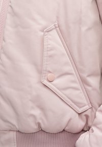 Tessuto per giubbotto bomber di colore rosa chiaro con finitura testurizzata, dotato di una tasca laterale con bottone rotondo e orlo e polsini a coste.