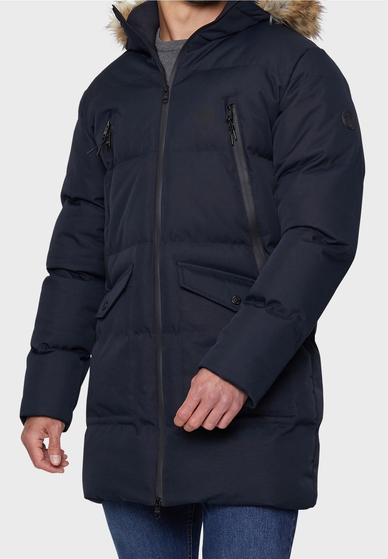 Navyblauwe gewatteerde parka-jas met een capuchon van nepbont, twee borstzakken met rits en twee knoopzakken aan de voorkant; voorzien van een stevige ritssluiting.