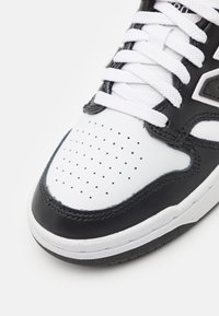 Gros plan sur l'avant d'une basket noire et blanche avec du cuir blanc perforé, un liseré noir, des lacets blancs et une semelle texturée.