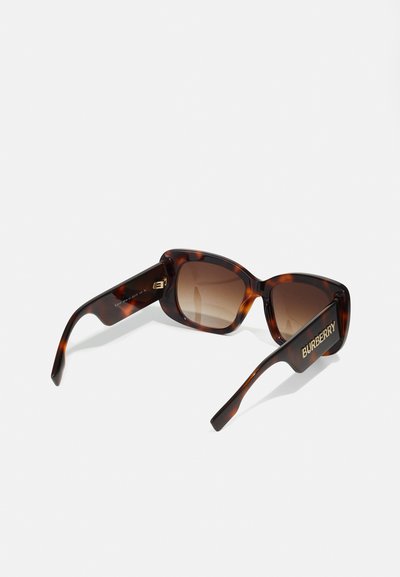 Brūni ķīļveida saulesbrilles ar taisnstūra rāmi, gradienta lēcas un zelta "Burberry" zīmējumu uz tempļiem. Gluda tekstūra, mūsdienīgs dizains.