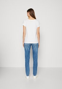 Weißes Baumwoll-T-Shirt mit kurzen Ärmeln und Rundhalsausschnitt, kombiniert mit hellblauen Jeans, von hinten gezeigt.