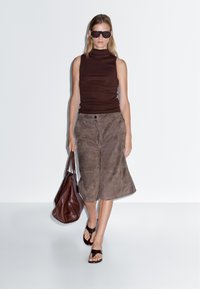 Bruine mouwloze coltrui, suède bruin culottebroek, bruine sandalen en een grote bruine tas. Minimalistisch ontwerp, zachte textuur.