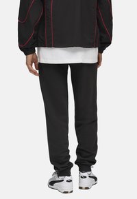 Sorte sweatpants lavet af blødt stof, med en afslappet pasform og ribbede manchetter, parret med hvide træningssko og et lagdelt outfit.