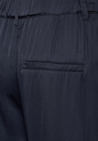 Primo piano di pantaloni blu scuro che mostrano una tasca a filetto posteriore e una cintura elastica con passanti per cintura.