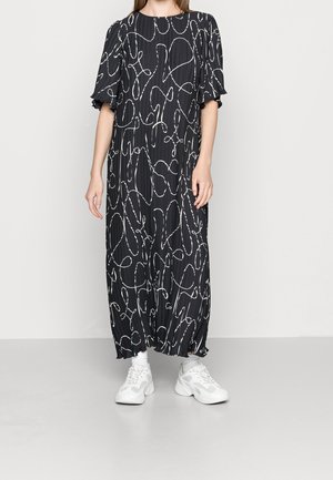 Mujer con vestido midi negro con líneas abstractas blancas y mangas abullonadas, combinado con zapatillas blancas gruesas y calcetines blancos.