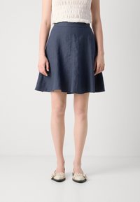 Navy blue A-line skirt in textured fabric, featuring a high waist and frayed hem. Paired with light-colored flat shoes.