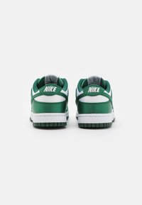 Nike Dunks s zeleným saténovým svrškem, bílými koženými detaily, texturovanými tkaničkami a zelenou gumovou podrážkou. Logo je umístěno na patě.