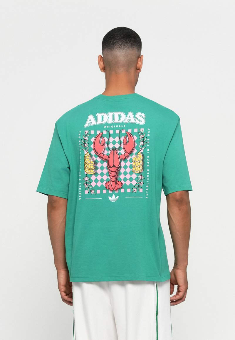 Türkiz színű pamut póló, rózsaszín homárral, kockás mintával, és "ADIDAS ORIGINALS" felirattal a hátsó részén. Rövid ujjú.