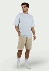 Light blue, textured short-sleeve shirt paired with beige knee-length shorts featuring diagonal stripes. White sneakers and socks complete the look.