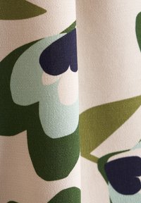 Tessuto con un motivo floreale caratterizzato da grandi foglie in tonalità di verde e blu su uno sfondo crema, superficie texturizzata.