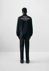 Black work jacket and pants, featuring embroidered logos on the back. The jacket has a collared design and snap closures, with textured fabric.