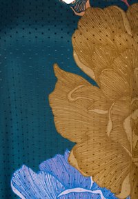 Tessuto con uno sfondo verde scuro e una trama textures, decorato con grandi disegni floreali in oro e blu che evidenziano dettagli intricati.