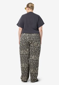 T-shirt oversize gris associé à un pantalon large beige à motifs zèbres. Les pantalons présentent un imprimé texturé avec une coupe ample et fluide. Chaussures noires.