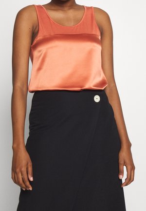 Débardeur en satin couleur orange brûlé avec un décolleté bateau, associé à une jupe portefeuille noire dotée d'une accent de bouton blanc.