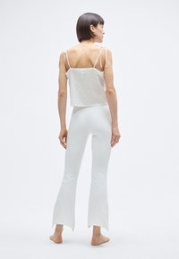 Haut court blanc avec bretelles à nouer réglables, tissu texturé. Assorti à un pantalon évasé blanc avec ourlet brut. Le mannequin est pieds nus.