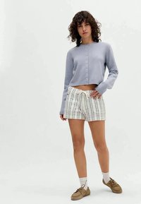 Lys lilla kort cardigan med knapper, kombinert med hvite og stripete shorts. Enkel design, bomullstekstur og nøytrale brune sko.